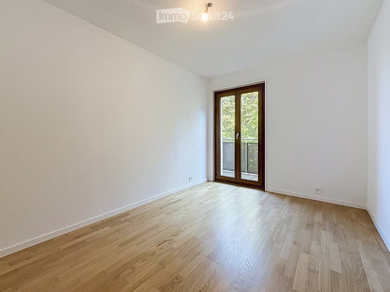 Empty room with light wooden flooring, white walls, and a large sliding glass door leading to a balcony.