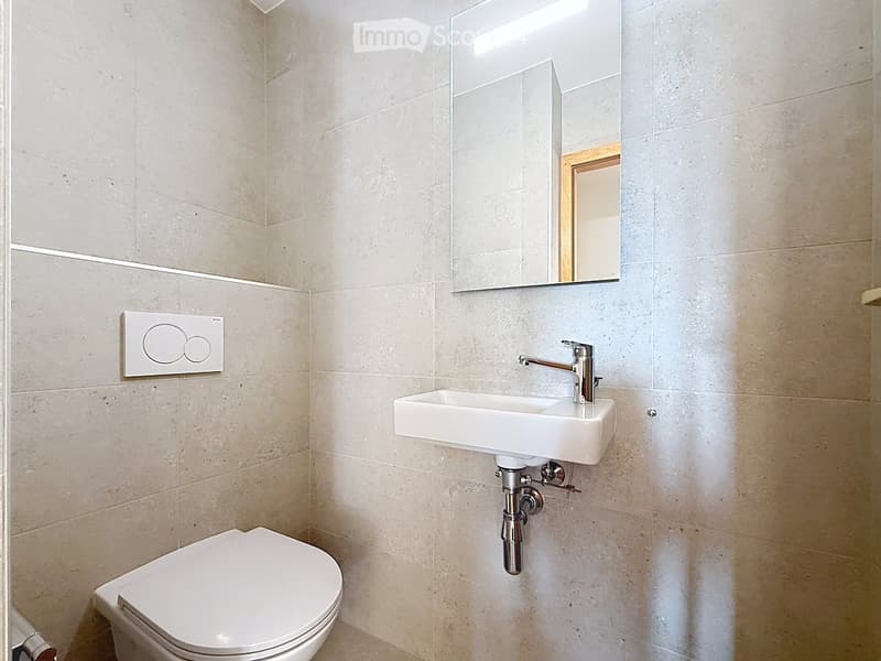 Modern bathroom with beige tiled walls, a white toilet, a white sink with a chrome faucet, and a rectangular mirror above the sink.