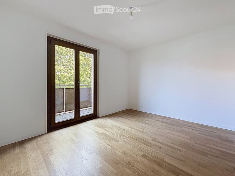 Empty room with light wooden flooring, white walls, and a large sliding glass door leading to a balcony.
