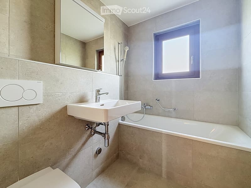 Modern bathroom with beige tiles, a white sink, a bathtub, a mirror, and a toilet.