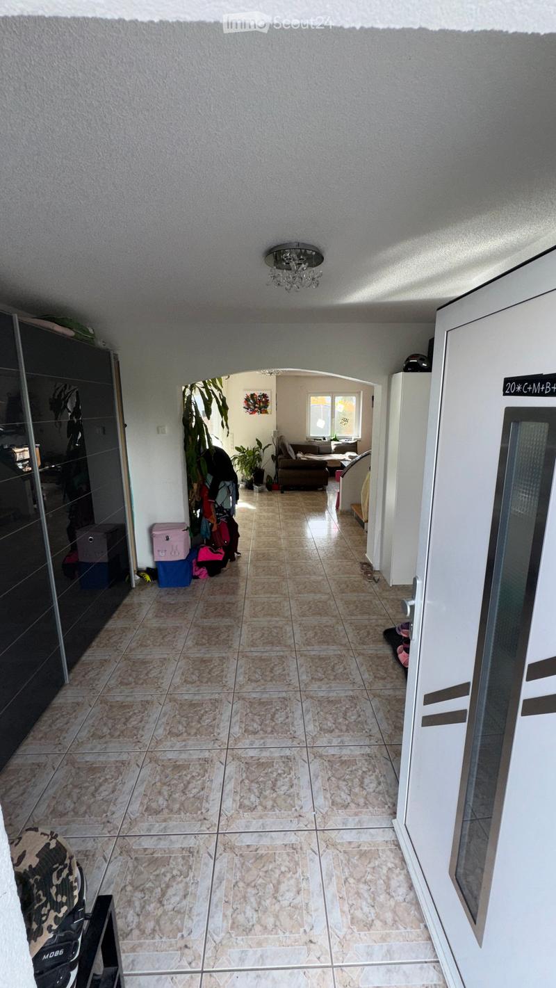 Hallway with tiled floor, leading to a living area with a sofa and coffee table, visible plants, and storage items along the walls.