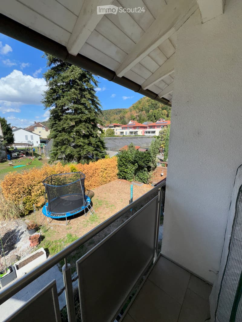 Balcony overlooking a garden area with a trampoline, surrounded by trees and neighboring houses.