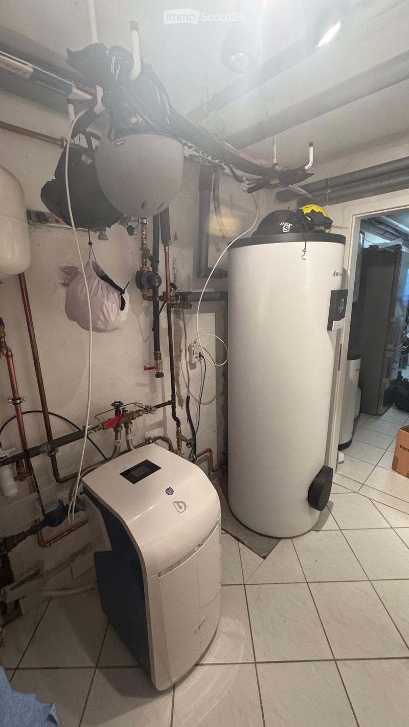 Utility room with water heater, thermostat, and various pipes.