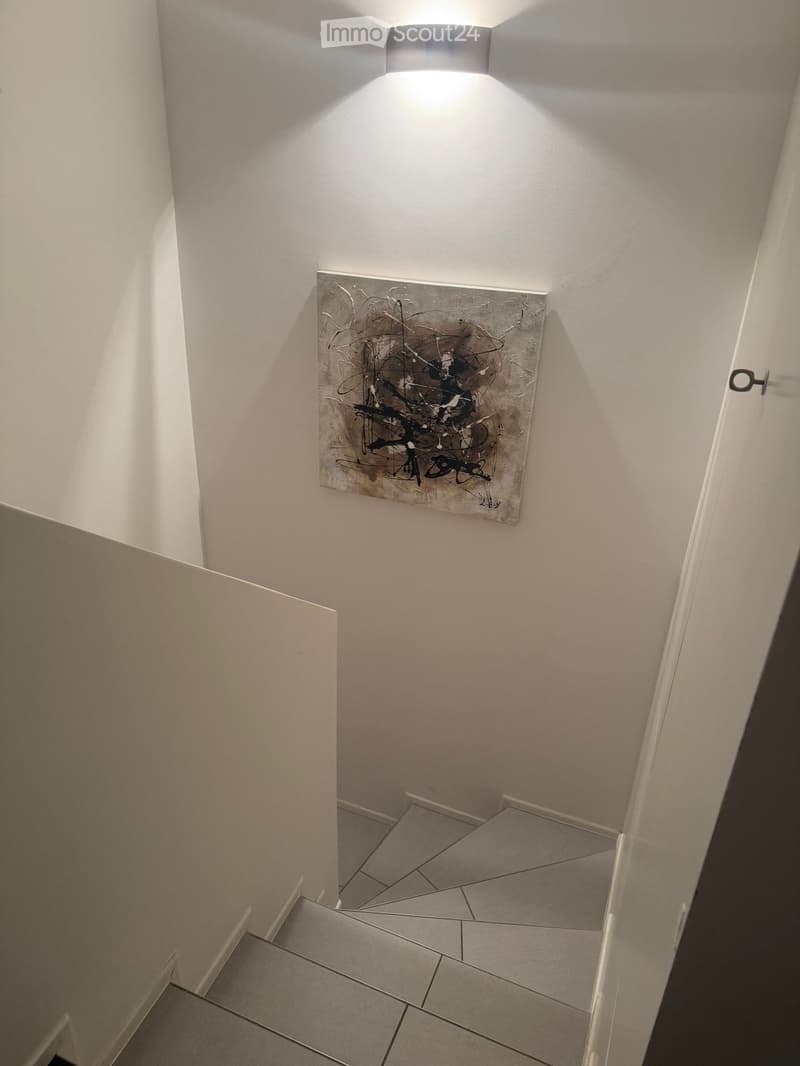 Modern hallway with tiled floor, white walls, a modern light fixture, and an abstract painting on the wall.