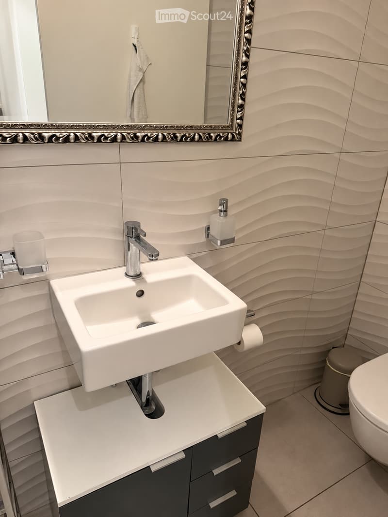 Modern bathroom with a white sink, chrome faucet, mirrored cabinet, and sleek black cabinetry.