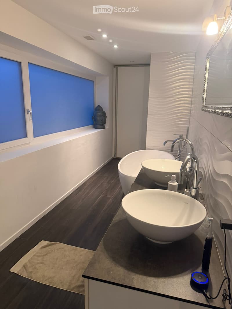 Modern bathroom with a large bathtub, two sinks, a mirror, and a decorative Buddha head on the windowsill.