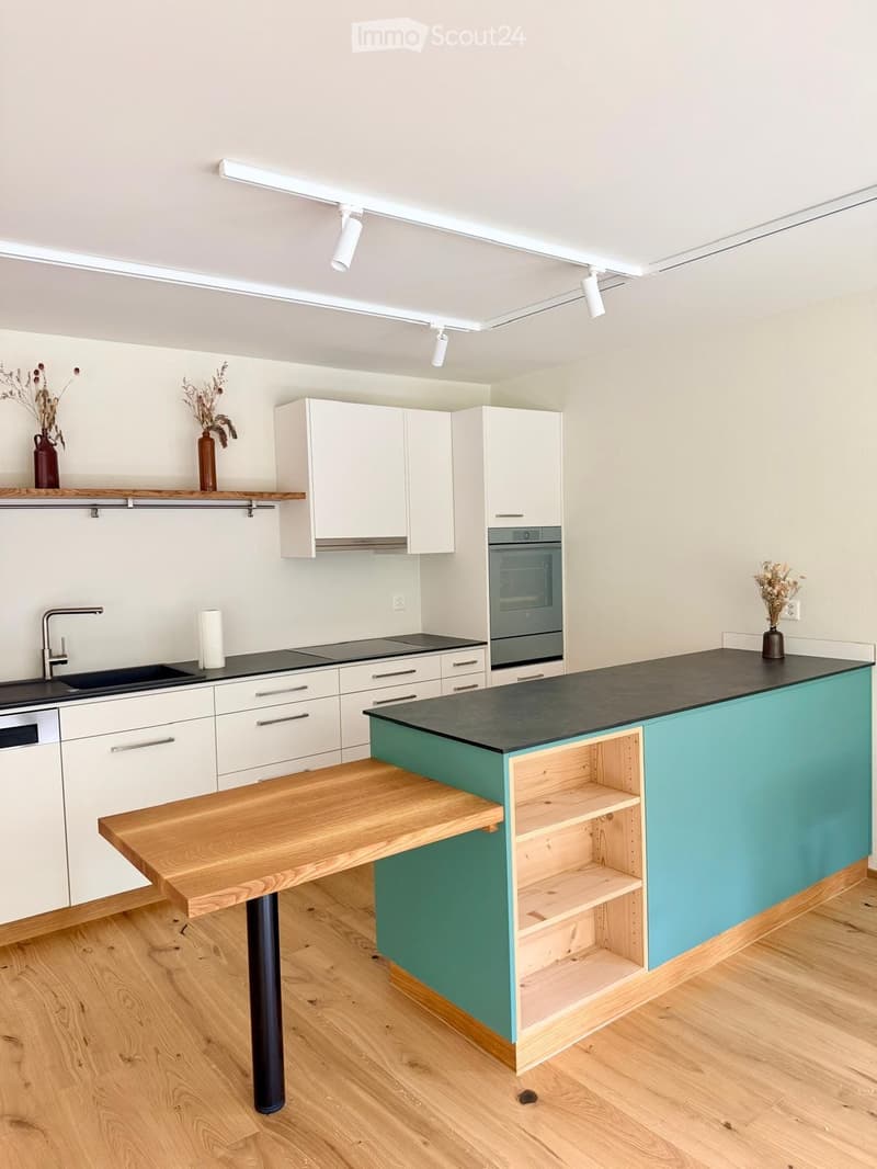 Modern kitchen with white cabinets, black countertop, wooden island, sink, and oven.