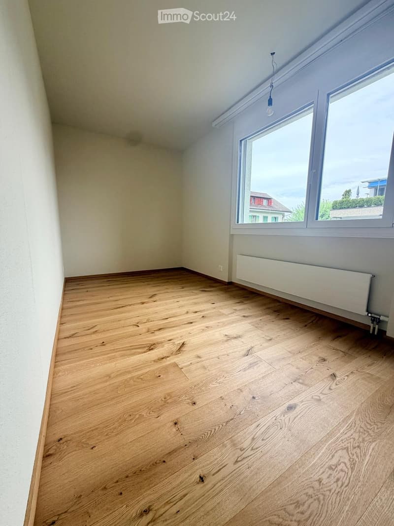 Empty room with wooden flooring, white walls, and a large window with a radiator below it.