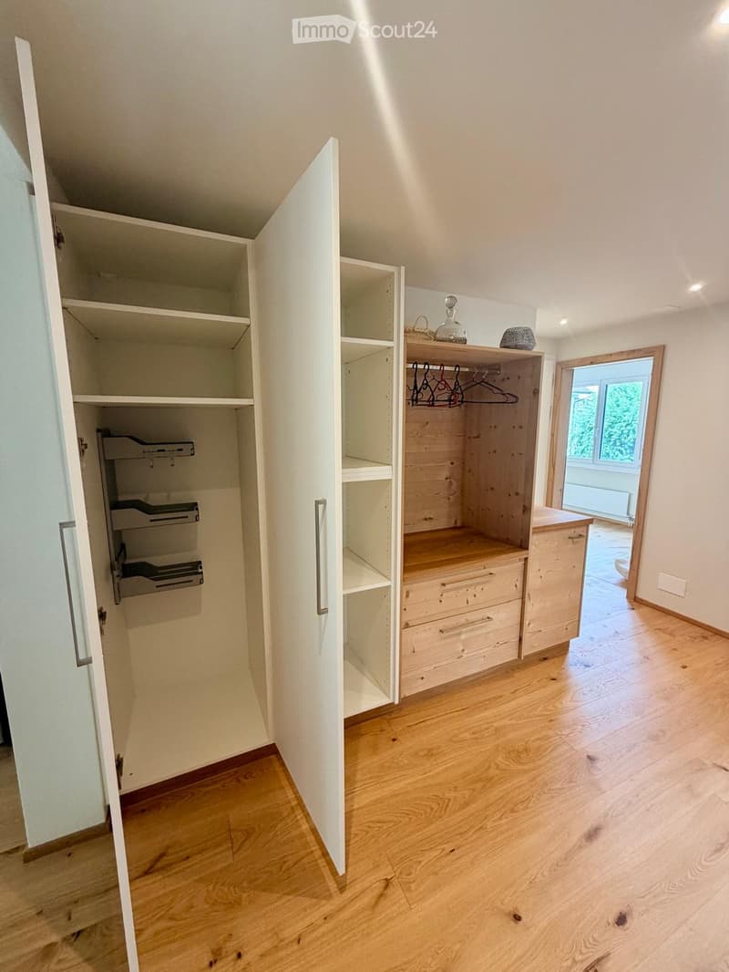 Empty room with wooden flooring, white walls, built-in wardrobes with open shelving and drawers, and a small window letting in natural light.