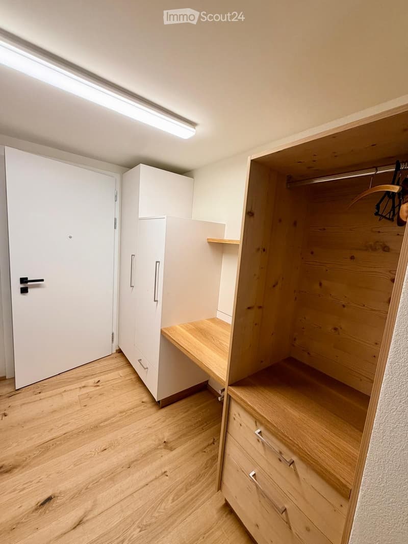 Empty room with wooden flooring, white walls, built-in white cabinets, and a wooden closet with open shelves and drawers.