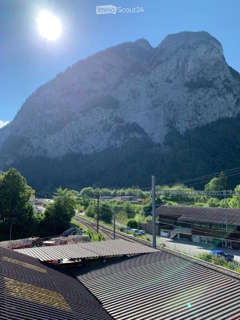 View from a rooftop showing a mountain range, railway tracks, and a small settlement below.
