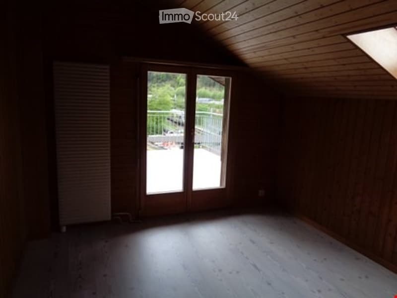 Empty attic room with wooden walls and floor, large skylight, and sliding glass door leading to a balcony.