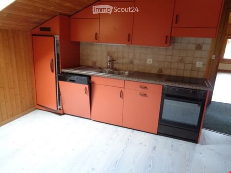A compact kitchen with orange cabinets, a refrigerator, dishwasher, oven, and a sink. The space features wooden walls and a light-colored floor.