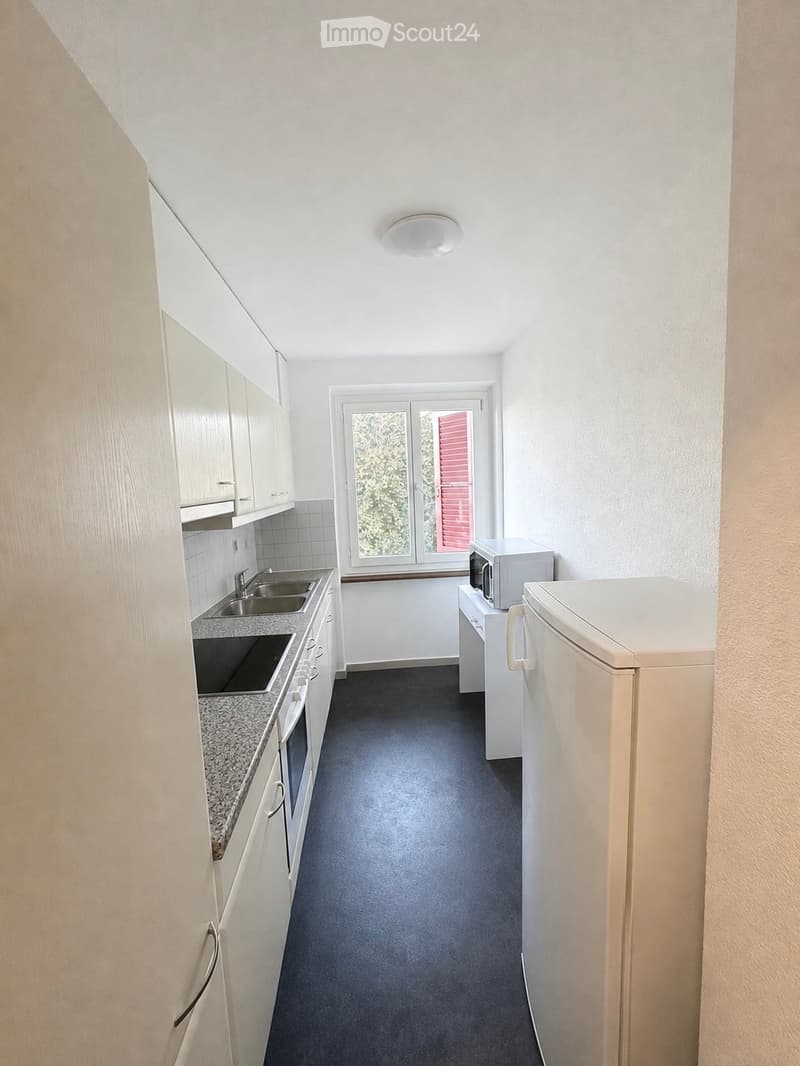 Modern kitchen with white cabinets, granite countertop, stainless steel sink, microwave, refrigerator, and oven. The room has a large window with a view of greenery.