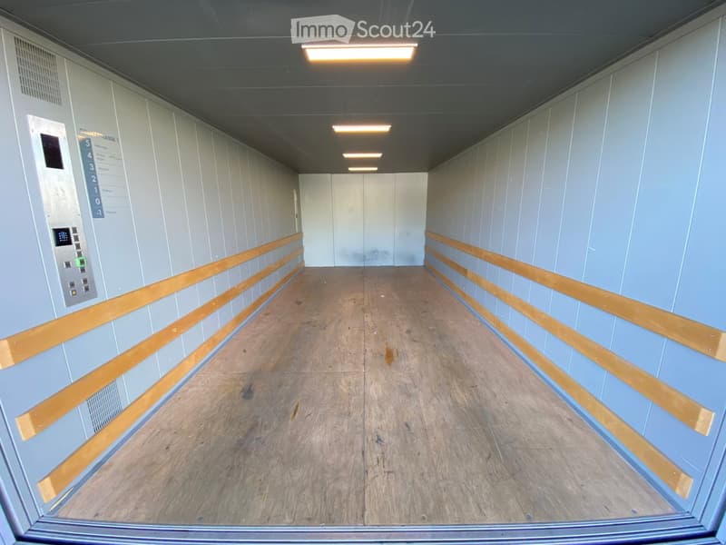 Empty hallway with light blue walls, wooden floor, and a control panel on the left side.