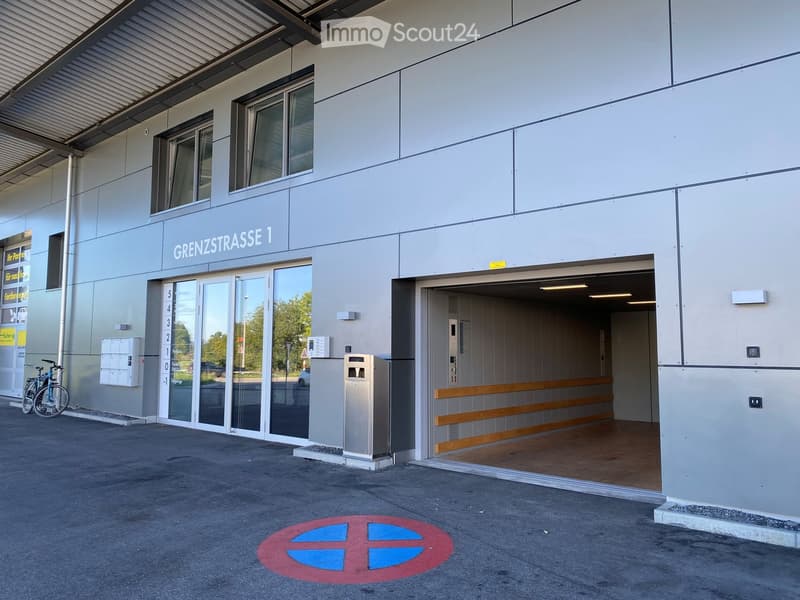 Modern building entrance with a raised ground floor, glass doors, bicycle parking, and a visible garage entrance.