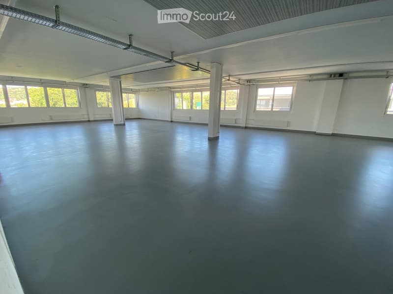 Empty room with white walls, large windows, and a dark grey floor. No furniture or equipment is present.
