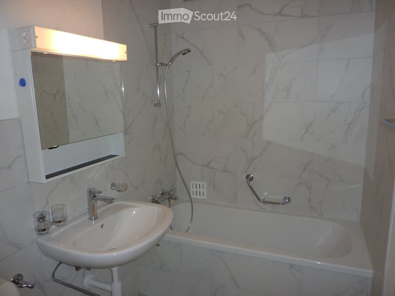 Modern bathroom with white tiles, bathtub, sink, shower head, mirror, and towel holder.