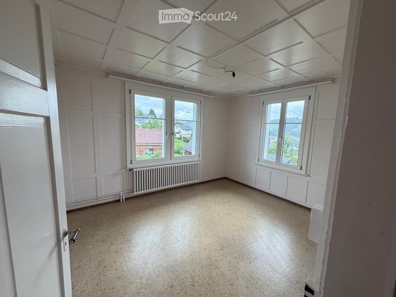 Empty room with white walls, carpeted floor, large windows, radiator, and a door.