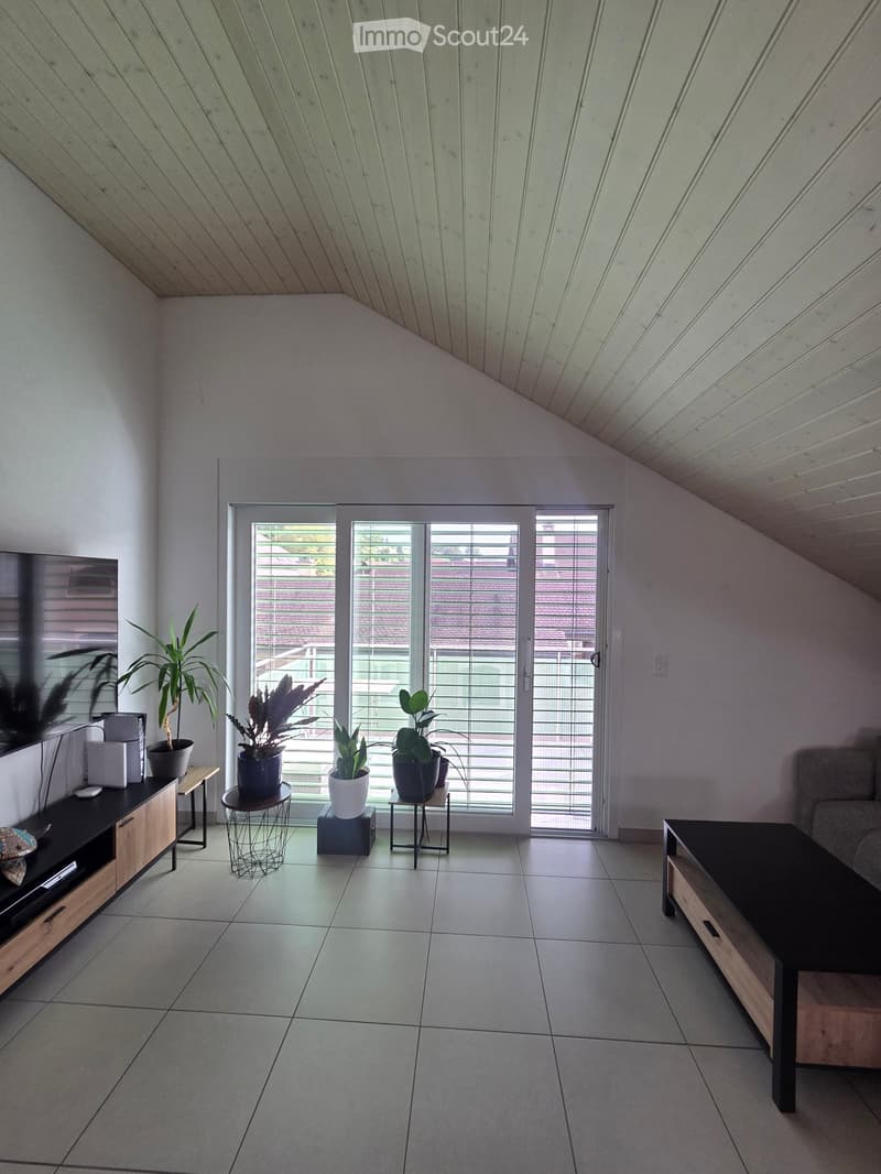 Modern living room with tiled floor, large sliding glass doors leading to a balcony, sofa, coffee table, side tables with potted plants, and a TV stand.