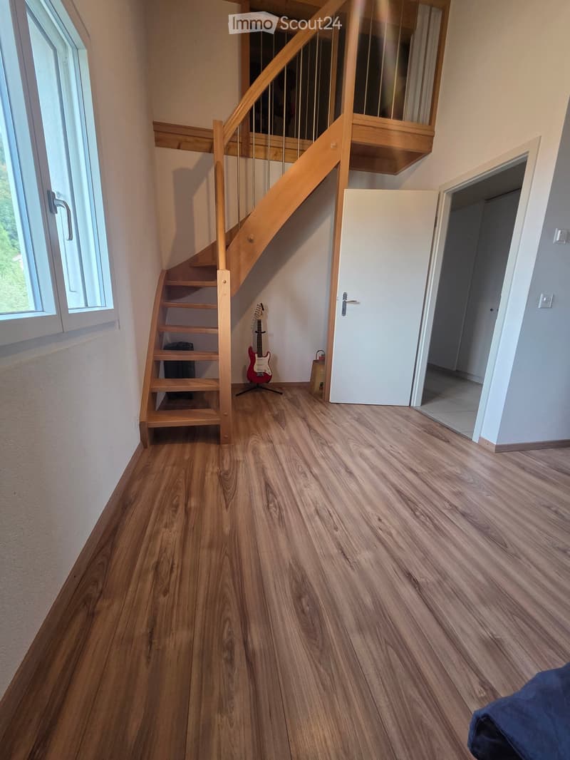 Spacious hallway with wooden flooring, a staircase leading to an upper level, and a guitar placed against the wall near the stairs.