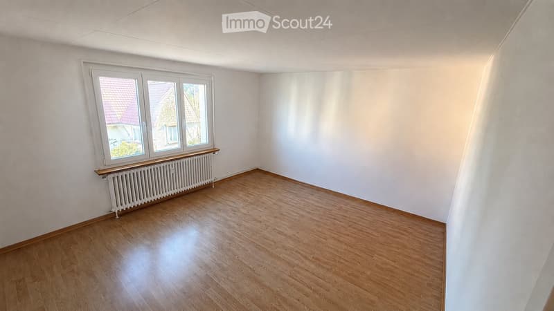 Empty room with wooden flooring, white walls, and a window with a radiator below it.