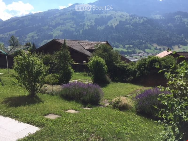 Well-maintained garden with green grass, lavender bushes, small trees, and a view of mountains in the background.