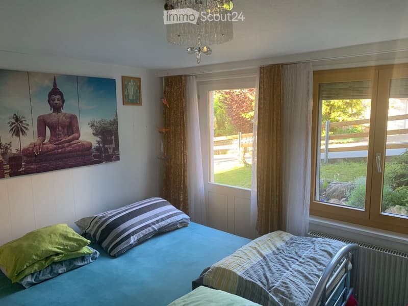 Cozy bedroom with a double bed, striped pillows, a chandelier, large windows with curtains, and a framed Buddha picture on the wall.