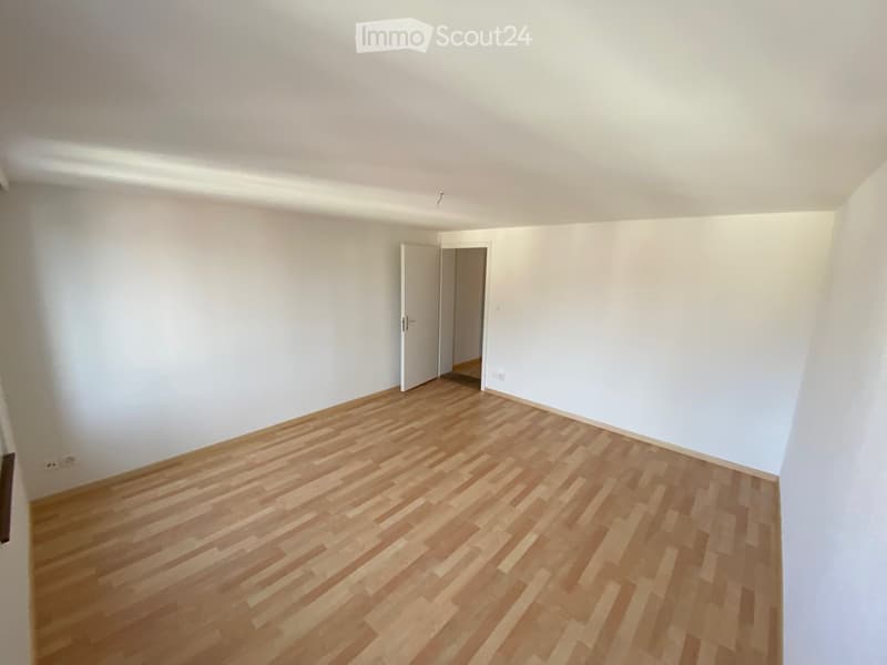 Empty room with light wooden flooring and white walls, featuring an open doorway leading to another space.