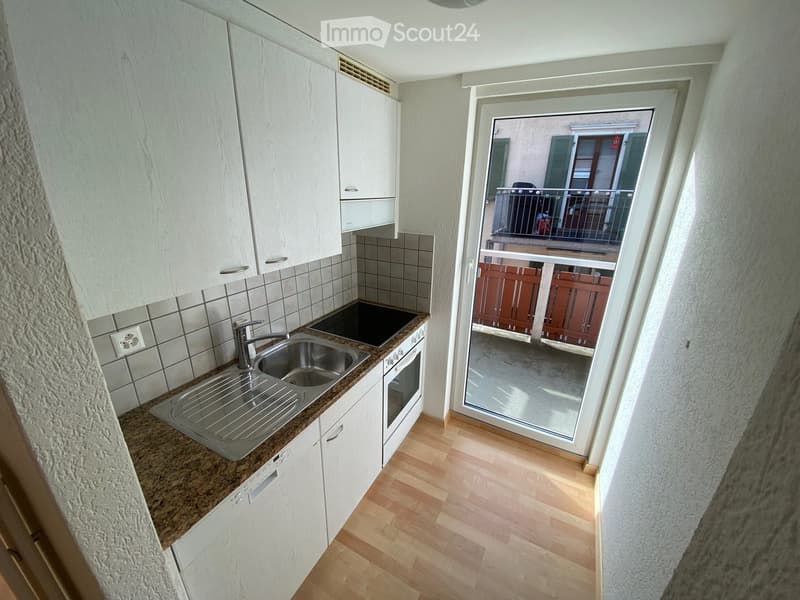 Modern kitchen with white cabinets, granite countertop, stainless steel sink, and a sliding glass door leading to a balcony.