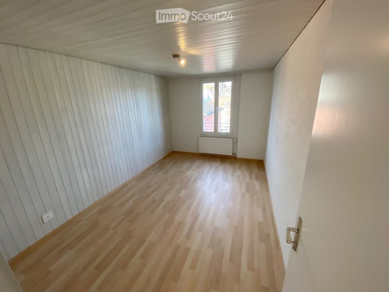 Empty room with wooden flooring, white walls, and a window with a radiator below it.