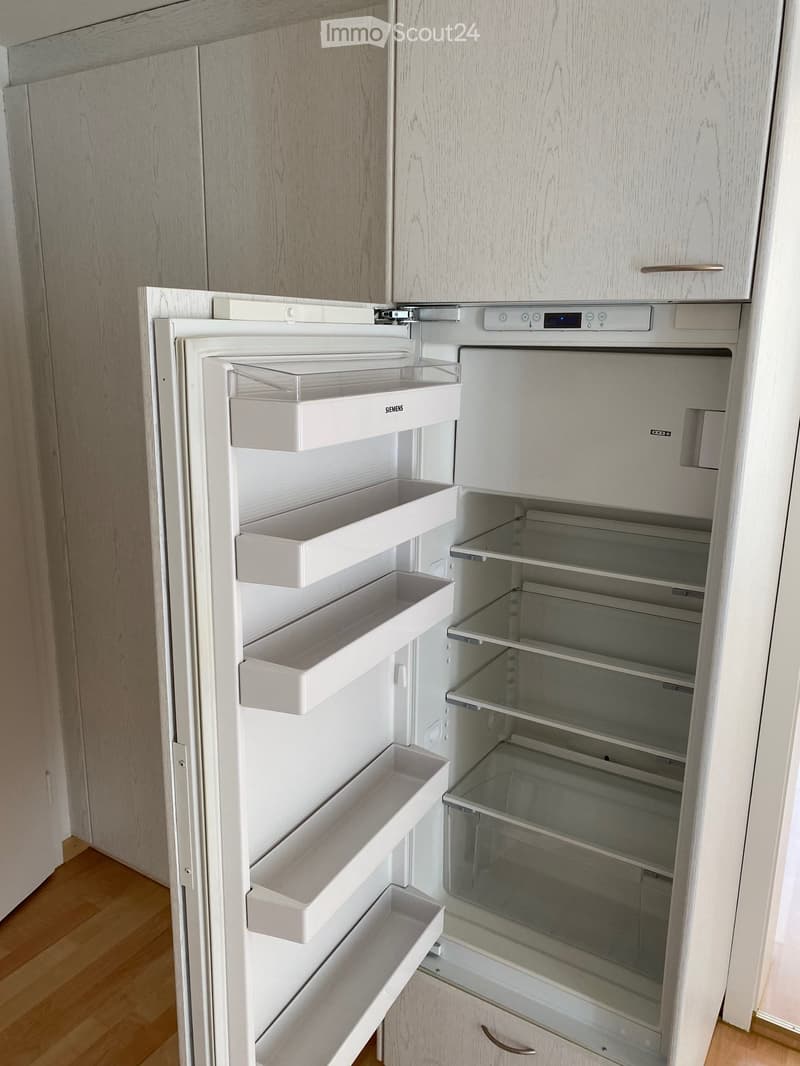 Modern kitchen with a white Siemens refrigerator, open with multiple shelves and compartments, integrated into light wood cabinetry.