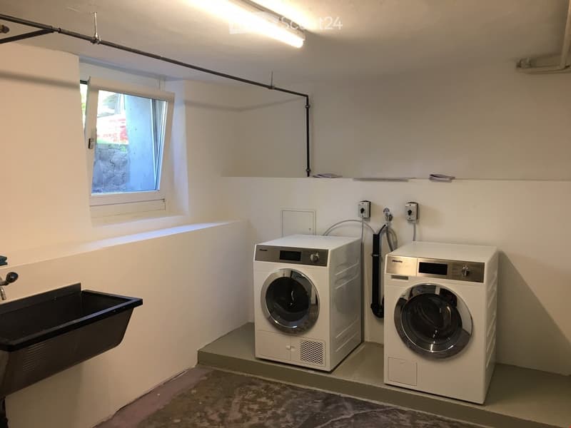 A laundry room with a window, two washing machines, and a sink.