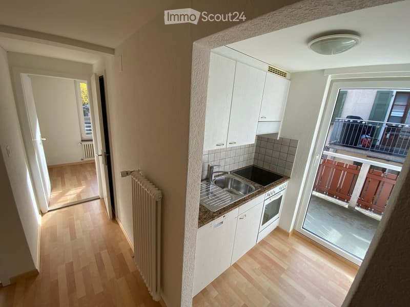 Modern kitchen with white cabinets, stainless steel sink, and a view to a balcony.