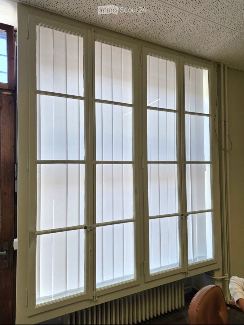 Empty room with large windows, radiator, and a partially visible chair in the corner.