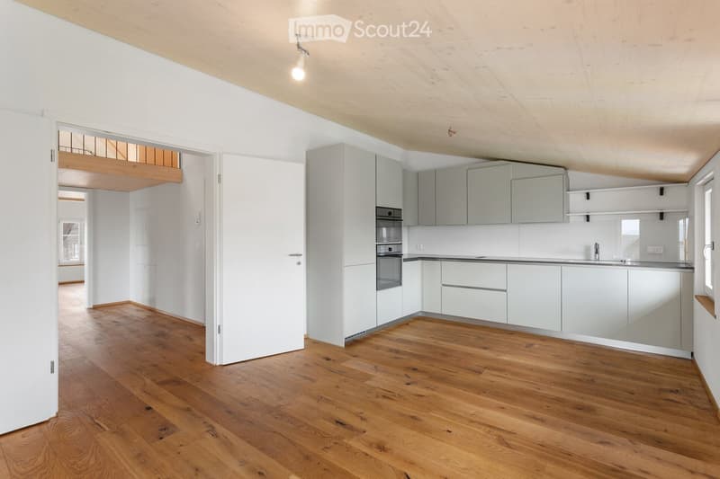 Modern kitchen with light grey cabinets, a built-in oven, and a sleek countertop. The space features wooden flooring and ample natural light from large windows.