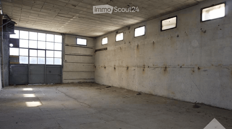 Empty industrial-style room with concrete walls and floor, large windows, and a metal door.