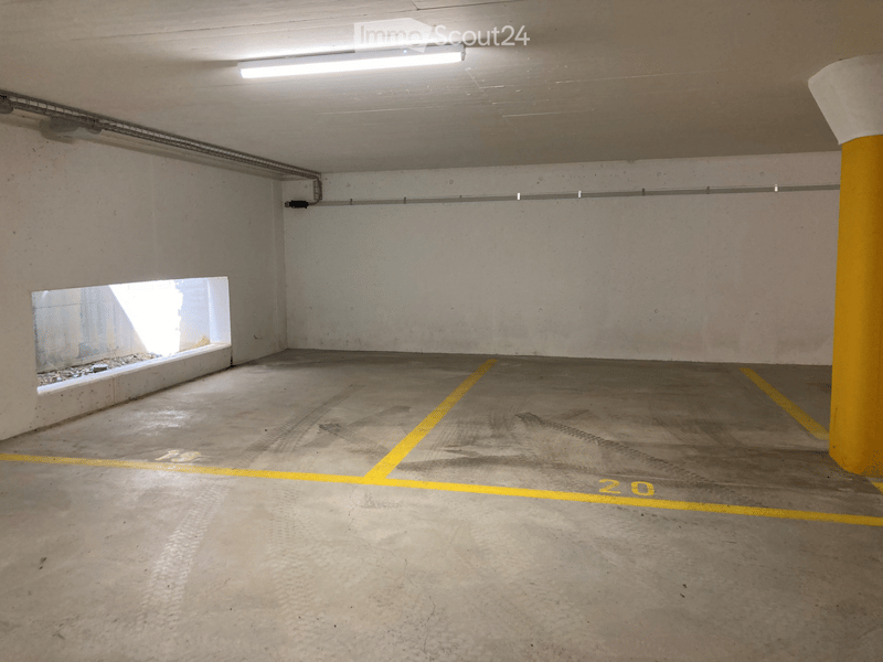 Underground parking space with concrete floors and walls, marked parking spots, and a single window providing natural light.