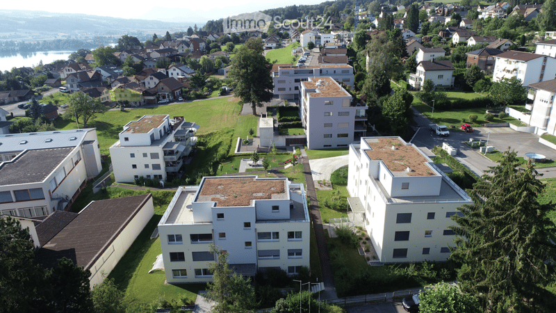Aerial view of a residential area with multiple apartment buildings, green spaces, parking lots, and a swimming pool.
