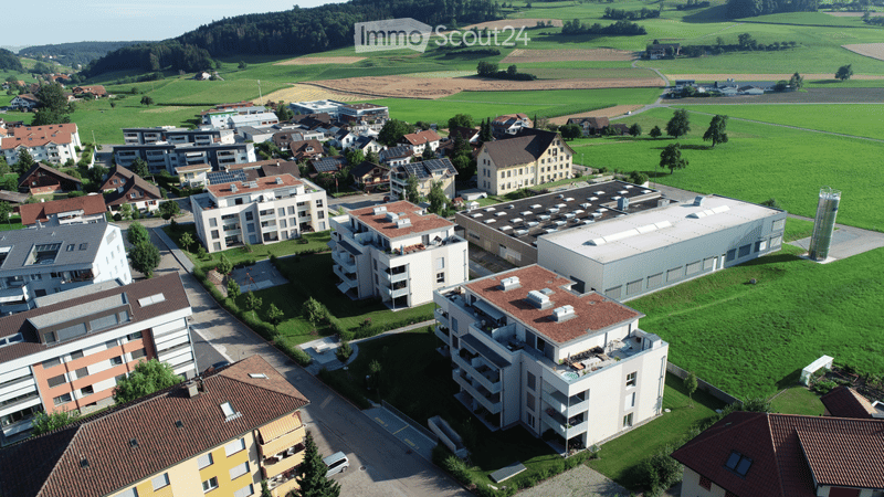Aerial view of a residential area with multiple apartment buildings, surrounded by green fields and scattered trees.