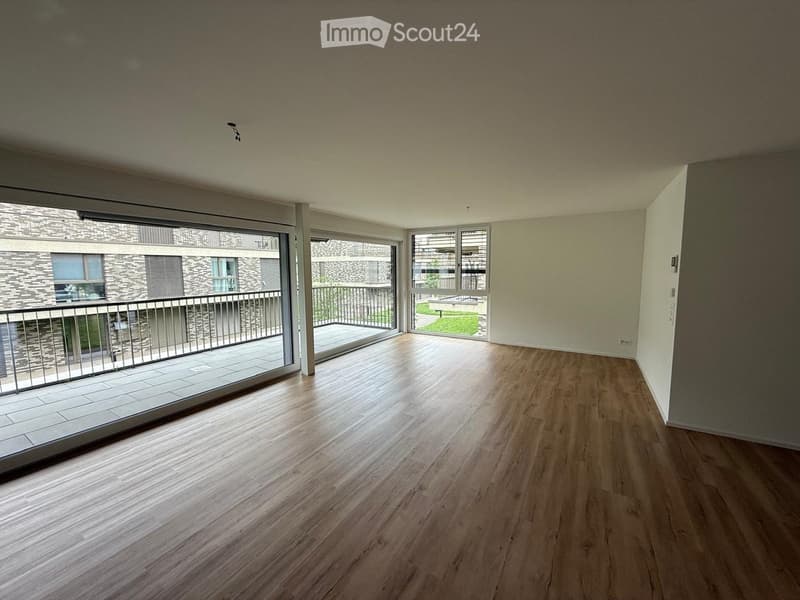 Empty room with wooden flooring, large sliding glass doors leading to a balcony, and white walls.