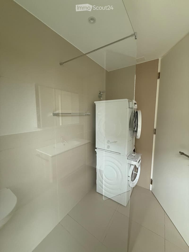 Modern bathroom with a glass-enclosed shower area, a white washing machine, and a white dishwasher stacked together.