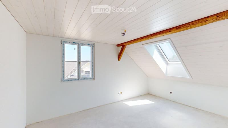 Empty attic room with white walls, wooden ceiling beams, and two windows (one standard and one skylight).