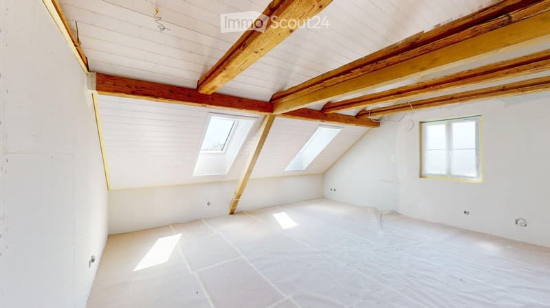 Empty attic space with exposed wooden beams, white walls, and skylights, featuring a tiled floor and natural light.