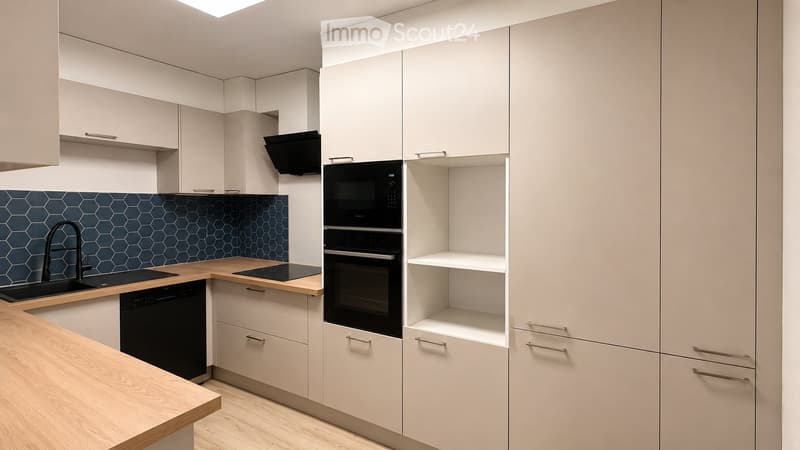 Modern kitchen with light-colored cabinets, a wooden countertop, and stainless steel appliances including an oven, microwave, and dishwasher. Features a hexagonal blue backsplash and a sleek faucet.