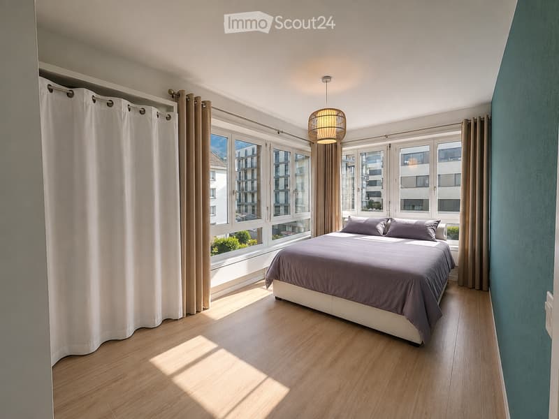 Bright bedroom with wooden flooring, large windows with white curtains, a modern bed with dark bedding, and a hanging woven light fixture.