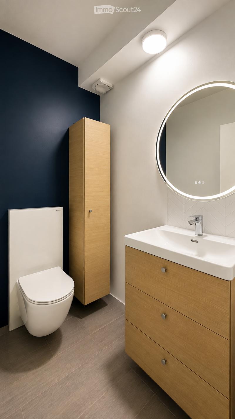 Modern bathroom with a white toilet, wooden cabinet, white sink with chrome faucet, and a round mirror with LED lighting.