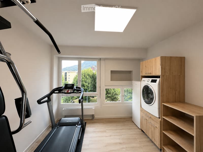 Well-lit room with wooden flooring, large windows offering a scenic view, a treadmill, a washing machine, and built-in wooden cabinetry.