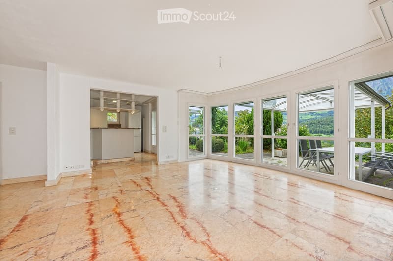 Bright, open room with large windows offering scenic views, featuring a wooden floor and a small seating area visible through the glass.