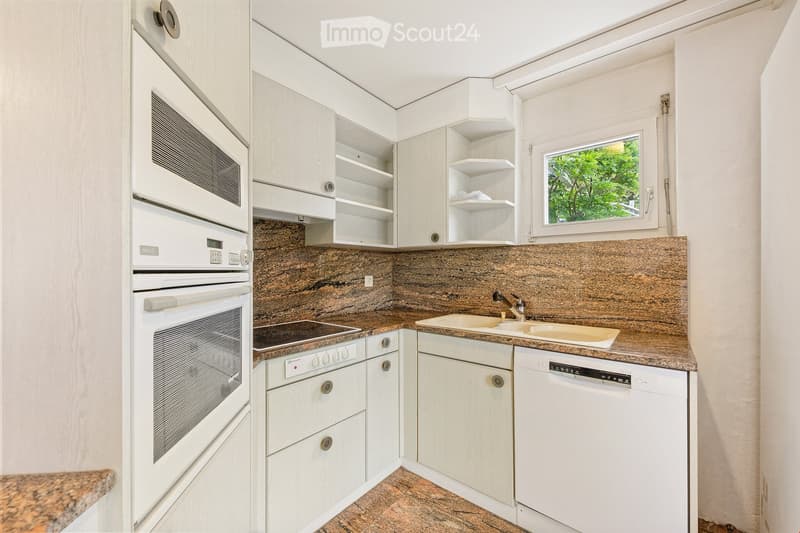 Modern kitchen with white cabinets, granite countertops, built-in oven, microwave, dishwasher, and a window overlooking greenery.